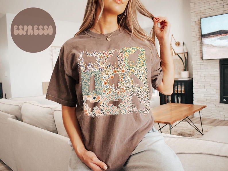 Op de afbeelding: Espresso-kleurig T-shirt met een bloemenontwerp. Het shirt heeft een rechthoekige afbeelding gevuld met een mix van kleurrijke bloemen en bladeren. Het woord "Espresso" is gedrukt in een cirkelvormige bruine vorm in de linkerbovenhoek. Het shirt heeft korte mouwen en een relaxte pasvorm.