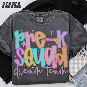 May include: Dark gray long-sleeve shirt with the words "Pre-K Squad Dream Team" in colorful bubble letters. The design includes flowers and stars. The word "Pepper" is at the top left.
