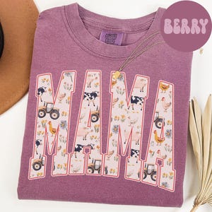 A purple t-shirt with the word "MAMA" printed on it, featuring various farm and animal-themed illustrations.