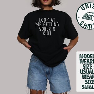 May include: Black t-shirt with white text that reads "Look at me getting sober & shit". The model is wearing a size L, but usually wears a size S.