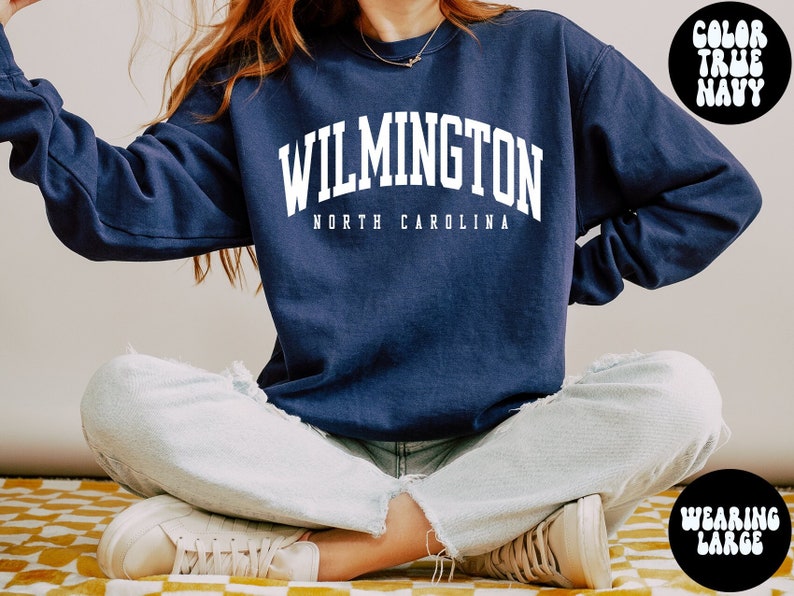 May include: A navy blue sweatshirt with the text "WILMINGTON NORTH CAROLINA" in white. The model is wearing a large size.