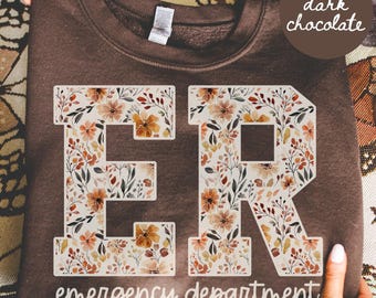 May include: Dark chocolate-colored sweatshirt with the letters "ER" in a floral design. The words "emergency department" are printed below the letters. The sweatshirt is a crew neck style.