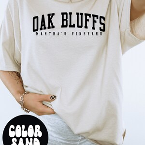 May include: A white t-shirt with black text that reads "OAK BLUFFS MARTHA'S VINEYARD". The shirt is oversized and has a relaxed fit.