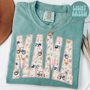 A turquoise t-shirt with the word "MAMA" printed on it, featuring various farm animals and farm-related elements.
