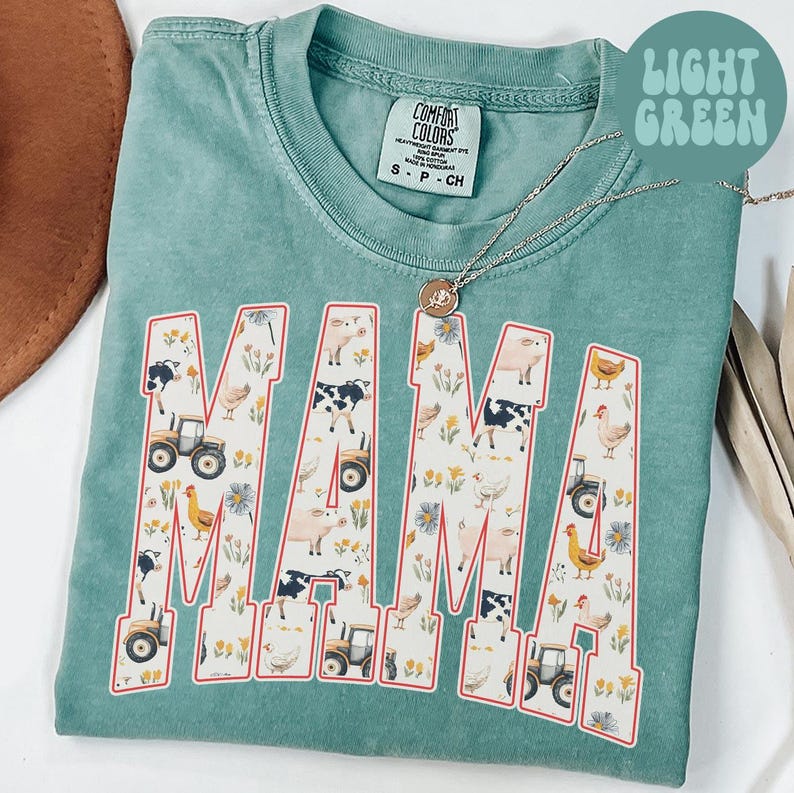 A turquoise t-shirt with the word "MAMA" printed on it, featuring various farm animals and farm-related elements.