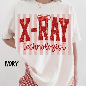 Könnte beinhalten: Elfenbeinfarbenes T-Shirt mit einem rot-rosa gestreiften Design. Das Shirt trägt die Worte "X-RAY technologist" in einer verblassten roten Schrift. Das Wort "IVORY" ist in schwarzer Schrift unten links auf dem Shirt aufgedruckt.