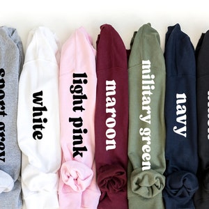 May include: Seven different colored sweatshirts with the color name printed on each in white text. The colors are sport grey, white, light pink, maroon, military green, navy, and black.
