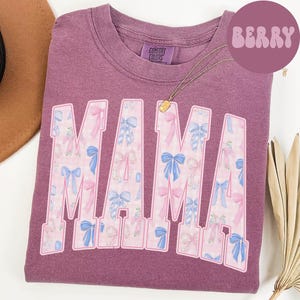 A purple t-shirt with the word "MAMA" printed in large letters, featuring a floral pattern in shades of pink and blue.