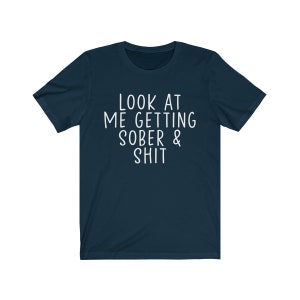 May include: A navy blue t-shirt with white text that reads "LOOK AT ME GETTING SOBER & SHIT".