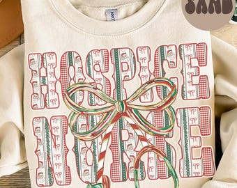 May include: Cream-colored sweatshirt with the words "HOSPICE NURSE" in a festive design. The letters are filled with Santa Claus and plaid patterns, and a large candy cane and bow graphic is in the center. The word "SAND" is in a circle in the upper right corner.