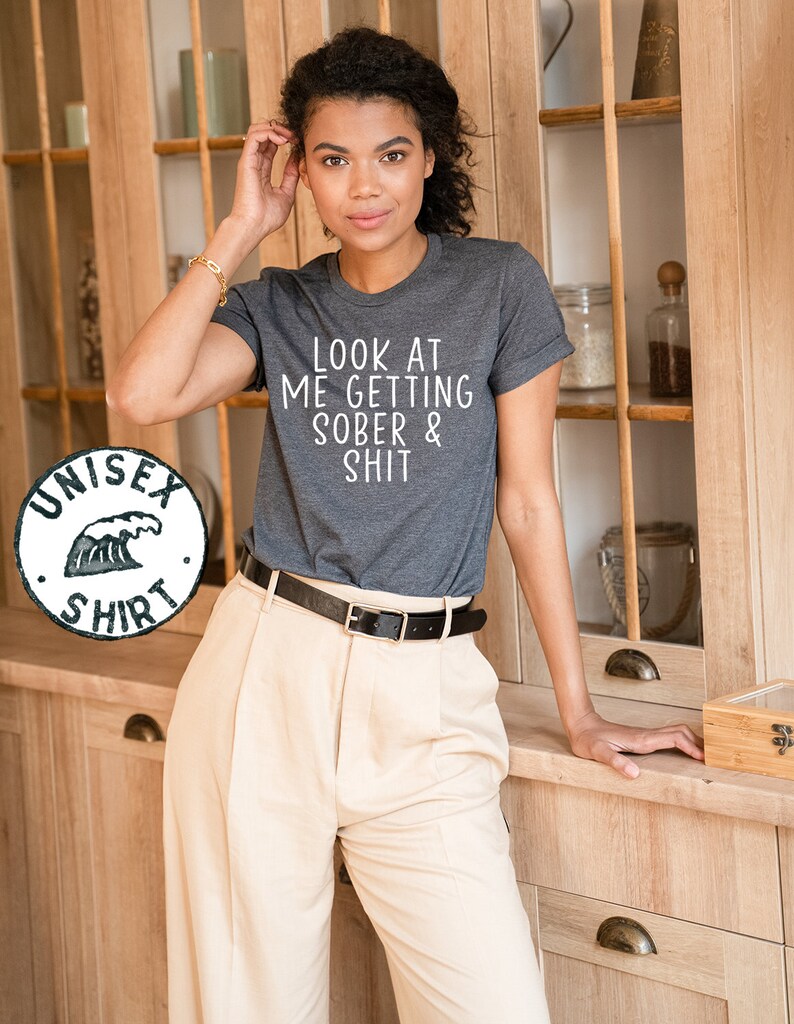 May include: A dark gray t-shirt with the text "LOOK AT ME GETTING SOBER & SHIT" printed in white.