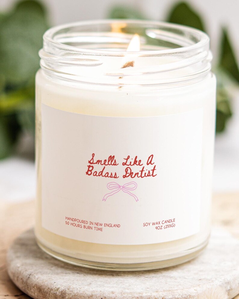 A white candle in a glass jar with a label that reads "Smells like a Badass Dentist".