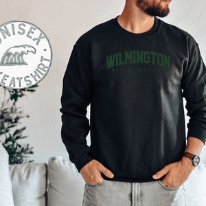 May include: Black sweatshirt with green text that reads "WILMINGTON NORTH CAROLINA". The sweatshirt is a unisex style.