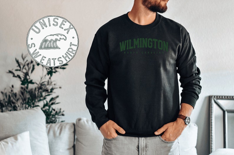 May include: Black sweatshirt with green text that reads "WILMINGTON NORTH CAROLINA". The sweatshirt is a unisex style.