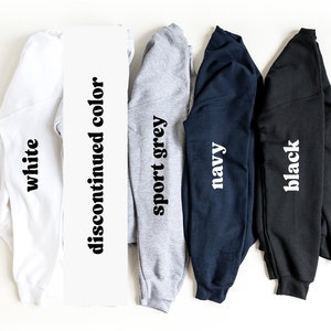 May include: Five long-sleeved shirts in different colors: white, sport grey, navy, black, and a discontinued color. The shirts are folded and laid out on a white surface.