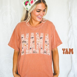 A smiling woman wearing a floral headband and a t-shirt with the word "MAM" printed on it.