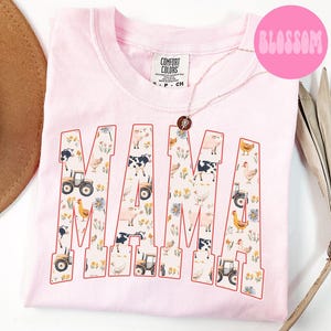 A pink t-shirt with the word "MAMA" printed on it, featuring various farm animals and farm-related elements.