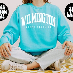 May include: A turquoise blue sweatshirt with the text "WILMINGTON NORTH CAROLINA" in white. The sweatshirt is a large size.