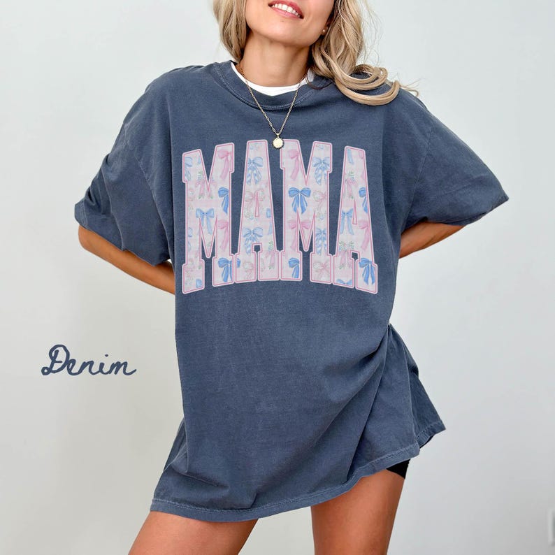 A woman wearing a blue t-shirt with the word "MAMA" printed on it, posing with her hands on her hips.