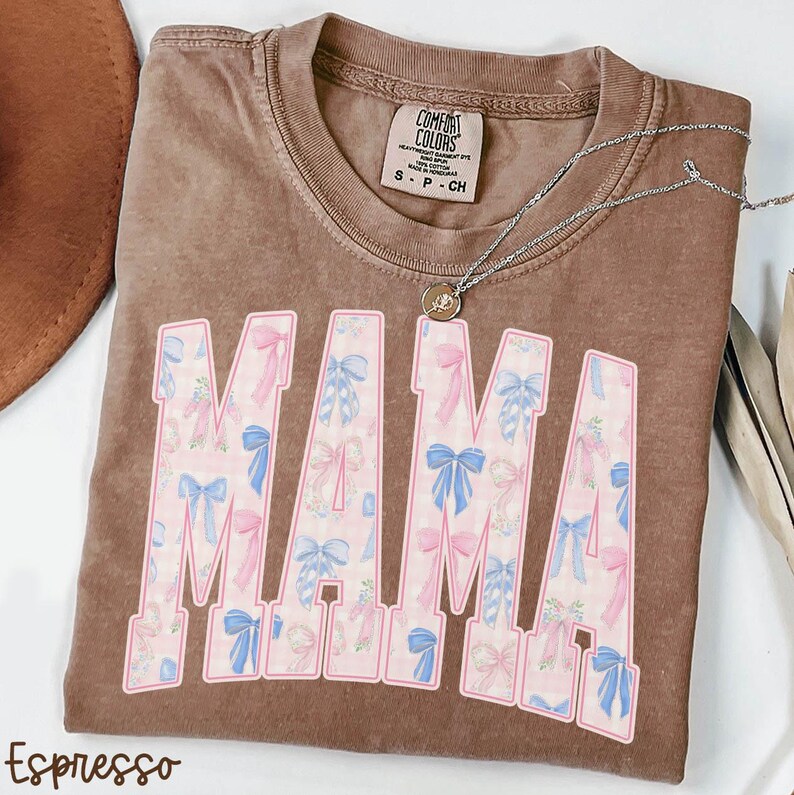 A brown t-shirt with the word "MAMA" printed in pink and blue letters, along with a necklace and a hat.