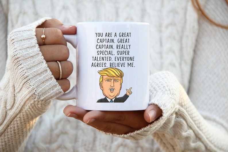 Puede incluir: Taza de caf&eacute; de cer&aacute;mica blanca con una imagen de dibujos animados de Donald Trump y el texto "YOU ARE A GREAT CAPTAIN. GREAT CAPTAIN. REALLY SPECIAL. SUPER TALENTED. EVERYONE AGREES. BELIEVE ME."