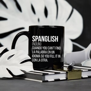 Pode incluir: Caneca de caf&eacute; preta com texto branco que diz "SPANGLISH (NOUN) CUANDO YOU CAN'T FIND LA PALABRA EN UN IDIOMA SO YOU FILL IT IN CON LA OTRA."