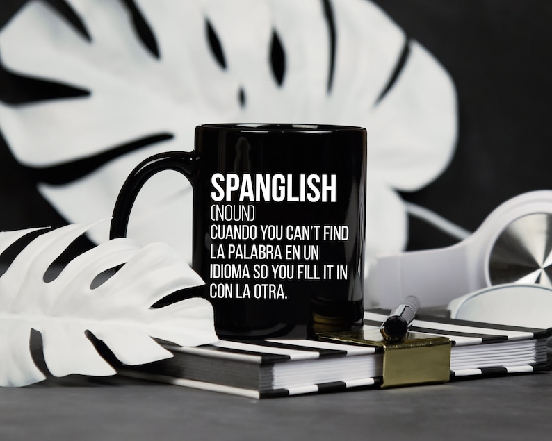 Pode incluir: Caneca de caf&eacute; preta com texto branco que diz "SPANGLISH (NOUN) CUANDO YOU CAN'T FIND LA PALABRA EN UN IDIOMA SO YOU FILL IT IN CON LA OTRA."