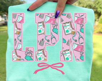 May include: A light teal sweatshirt with the letters "LPN" in pink, filled with medical-themed illustrations. A pink bow is at the bottom. The text "Island Reef" is at the bottom right.