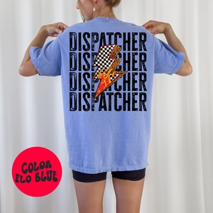 以下が含まれることがあります： 薄い青色のTシャツに、黒い文字で「DISPATCHER」という単語が4回繰り返されています。チェッカー柄、炎、ヒョウ柄のスタイリッシュな稲妻のグラフィックがTシャツの中央に配置されています。