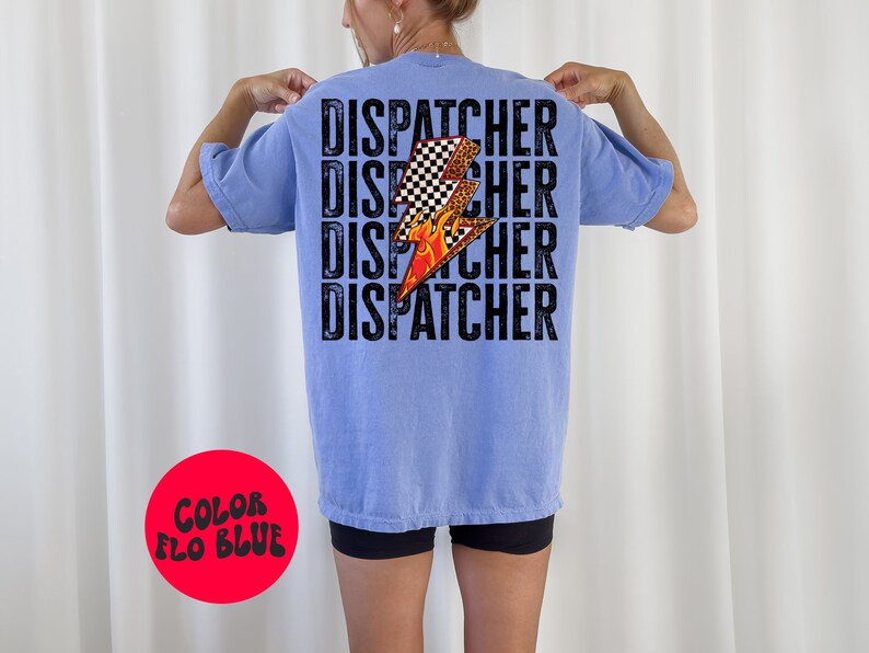 以下が含まれることがあります： 薄い青色のTシャツに、黒い文字で「DISPATCHER」という単語が4回繰り返されています。チェッカー柄、炎、ヒョウ柄のスタイリッシュな稲妻のグラフィックがTシャツの中央に配置されています。