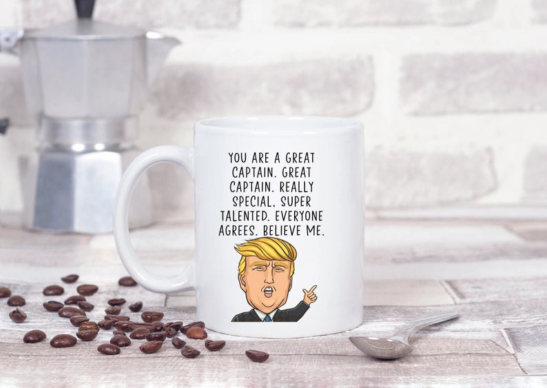 Puede incluir: Taza de caf&eacute; de cer&aacute;mica blanca con una imagen de dibujos animados de Donald Trump y el texto "YOU ARE A GREAT CAPTAIN. GREAT CAPTAIN. REALLY SPECIAL. SUPER TALENTED. EVERYONE AGREES. BELIEVE ME."