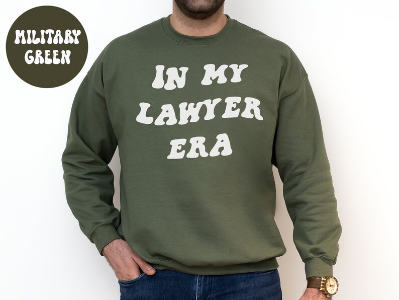 May include: A military green sweatshirt with the text "In My Lawyer Era" in white, retro-style lettering.