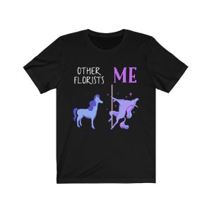 May include: Black t-shirt with a humorous graphic comparing other florists to a regular unicorn and the wearer to a unicorn doing a pole dance. The text reads "Other Florists" and "Me".