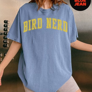 K&ouml;nnte beinhalten: Ein Oversize-T-Shirt in Jeansblau mit dem Text "BIRD NERD" in gelben Buchstaben.