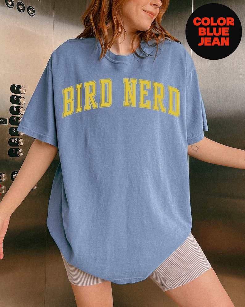 K&ouml;nnte beinhalten: Ein Oversize-T-Shirt in Jeansblau mit dem Text "BIRD NERD" in gelben Buchstaben.