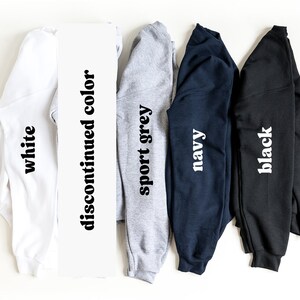 May include: Five long-sleeved shirts in different colors: white, sport grey, navy, black, and a discontinued color. The shirts are folded and laid out on a white surface.