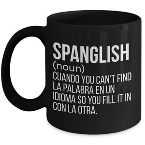Pode incluir: Caneca de caf&eacute; preta com um design branco que define o Spanglish como um substantivo. A defini&ccedil;&atilde;o diz: "CUANDO YOU CAN'T FIND LA PALABRA EN UN IDIOMA SO YOU FILL IT IN CON LA OTRA."