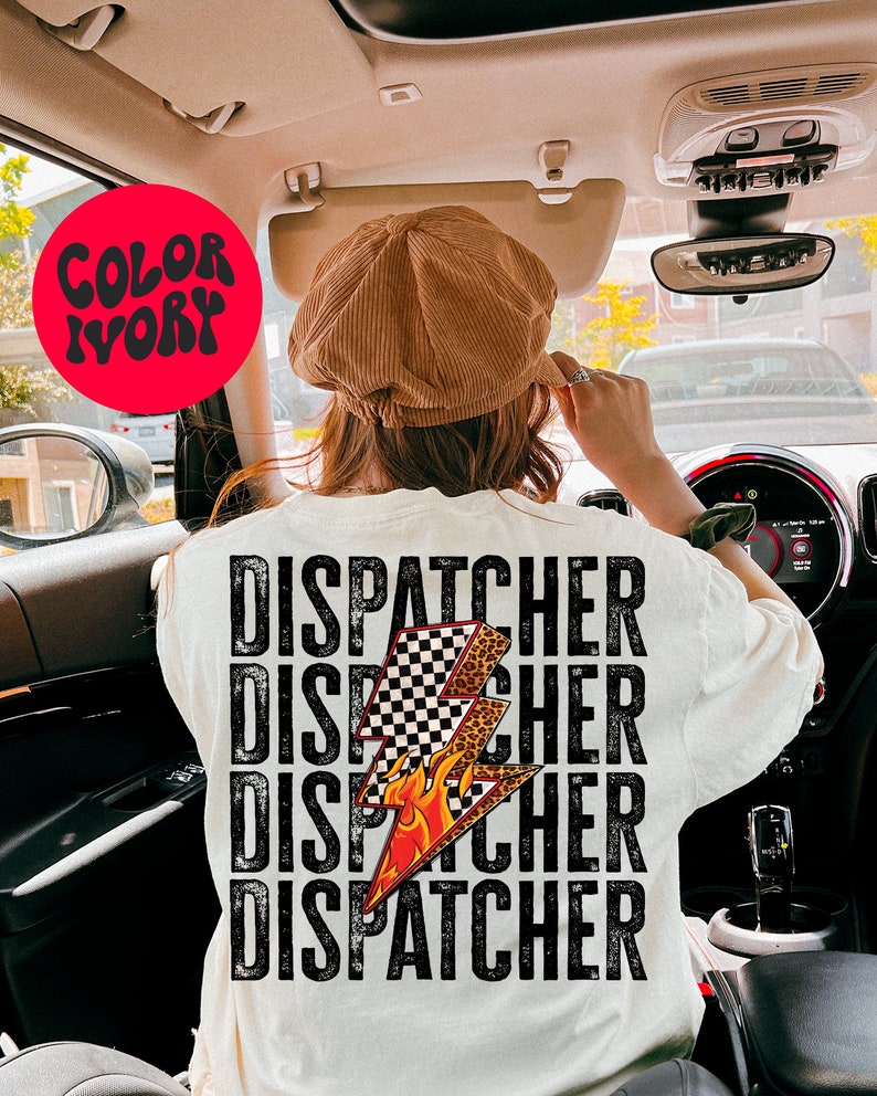 以下が含まれることがあります： 白いTシャツに、黒い文字で「DISPATCHER」という単語が4回繰り返されています。シャツの中央には、炎がついた黒と白の市松模様の稲妻が描かれています。