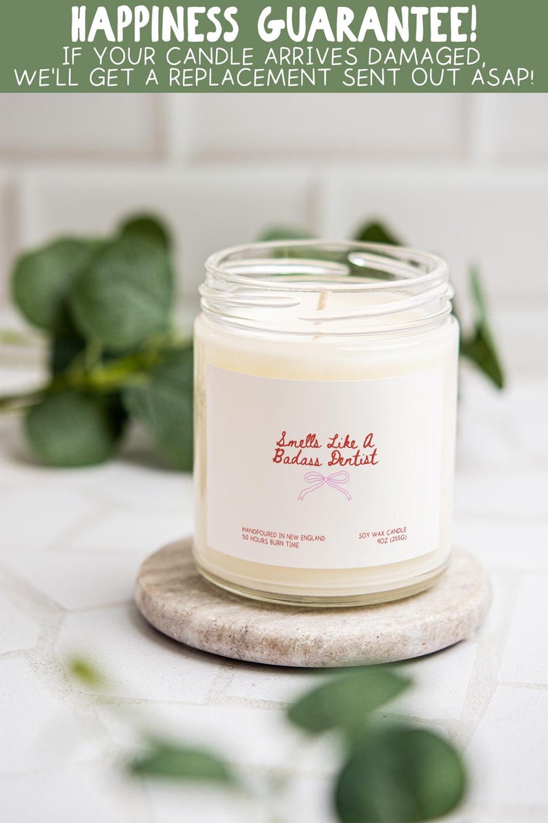 a white candle in a jar with a label that reads "Smells like a Badass Dentist", placed on a small stone coaster.