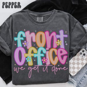 Puede incluir: Sudadera de manga larga gris oscuro con las palabras "front office we get it done" en letras coloridas y de burbujas. El texto está decorado con pequeñas flores y estrellas. La palabra "Pepper" está impresa en la parte superior.