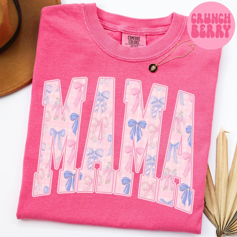 A pink t-shirt with the word "MAMA" printed in large letters, featuring a pattern of pink and blue bows.