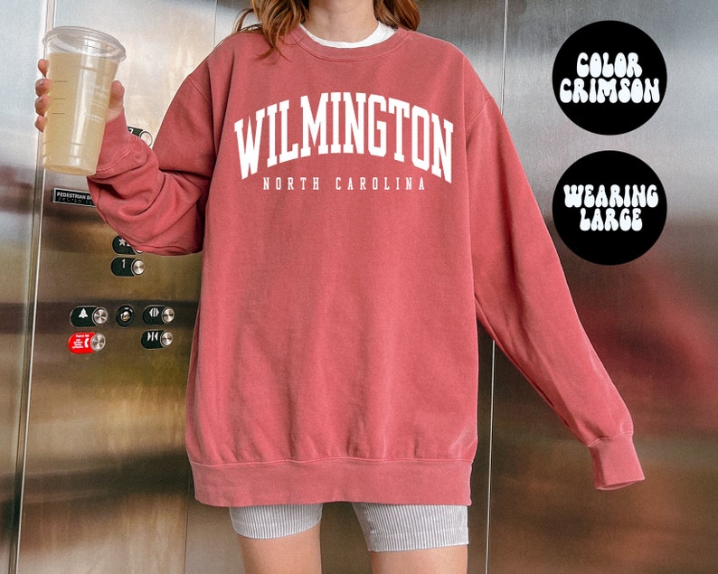 May include: A crimson coloured sweatshirt with the text "WILMINGTON NORTH CAROLINA" in white. The model is wearing a size large.