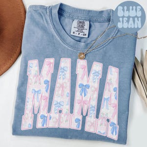 A blue t-shirt with the word "MAMA" printed in pink and blue bows, along with a necklace and a hat.
