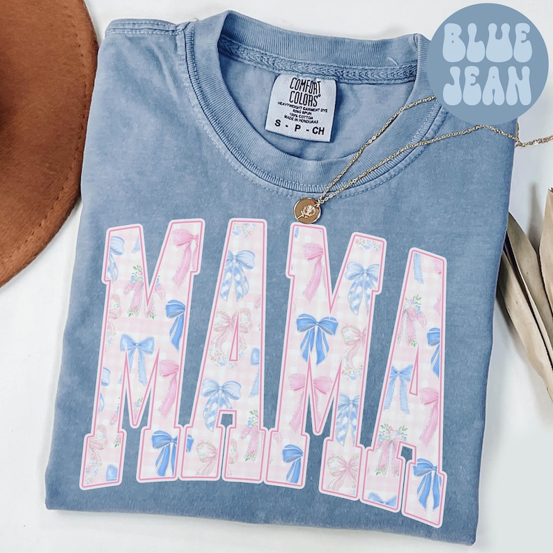 A blue t-shirt with the word "MAMA" printed in pink and blue bows, along with a necklace and a hat.