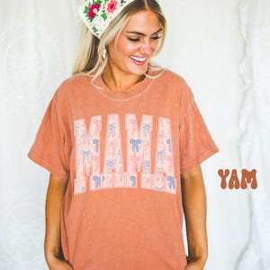 A smiling woman wearing a floral headband and a t-shirt with the word "MAM" printed on it.