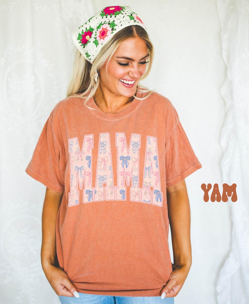 A smiling woman wearing a floral headband and a t-shirt with the word "MAM" printed on it.