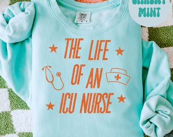 May include: A light blue sweatshirt with the text "THE LIFE OF AN ICU NURSE" in orange. The design includes a stethoscope, a nurse's hat, and stars. The words "Chalky Mint" are in a circle in the upper right corner.