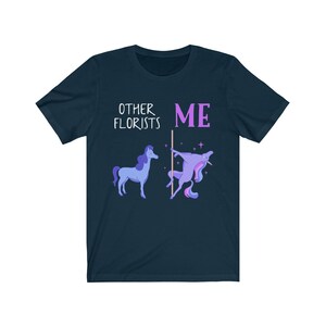May include: A navy blue t-shirt with the text "Other Florists" and a unicorn with a flower crown. The text "ME" is next to the unicorn, which is holding a pole.