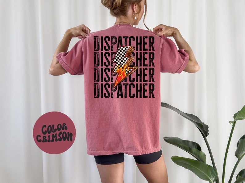 以下が含まれることがあります： 黒文字で「DISPATCHER」という単語が4回繰り返された、クリムゾンカラーのTシャツ。チェッカー柄と炎がついたスタイリッシュな稲妻のグラフィックがTシャツの中央に配置されています。
