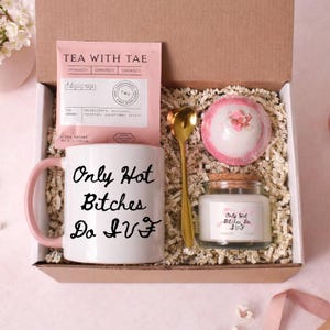 Könnte beinhalten: Geschenkbox mit einer weißen Tasse mit rosa Griff, einem Teebeutel, einem goldenen Löffel, einer Badekugel und einer Kerze. Auf der Tasse und der Kerze steht "Only Hot Bitches Do IVF". Der Teebeutel ist rosa und trägt die Aufschrift "Tea With Tae".
